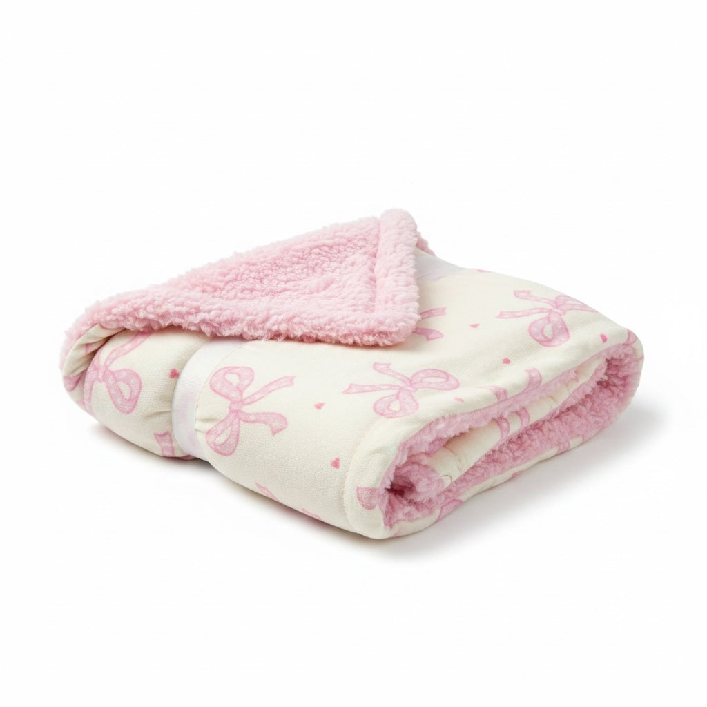 Manta Acüchichi para bebé con estampado de lazos rosas sobre fondo crema y reverso de textura borreguito suave