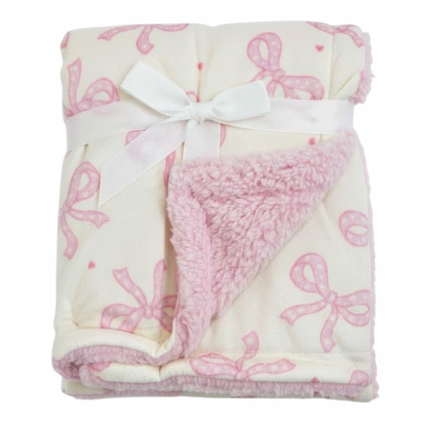 Manta Acüchichi para bebé con estampado de lazos rosas sobre fondo crema y reverso de suave borreguito rosa.